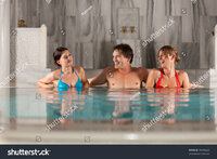 Stock photo three friends one man and two women in swimming pool or thermal bath doing wellnes